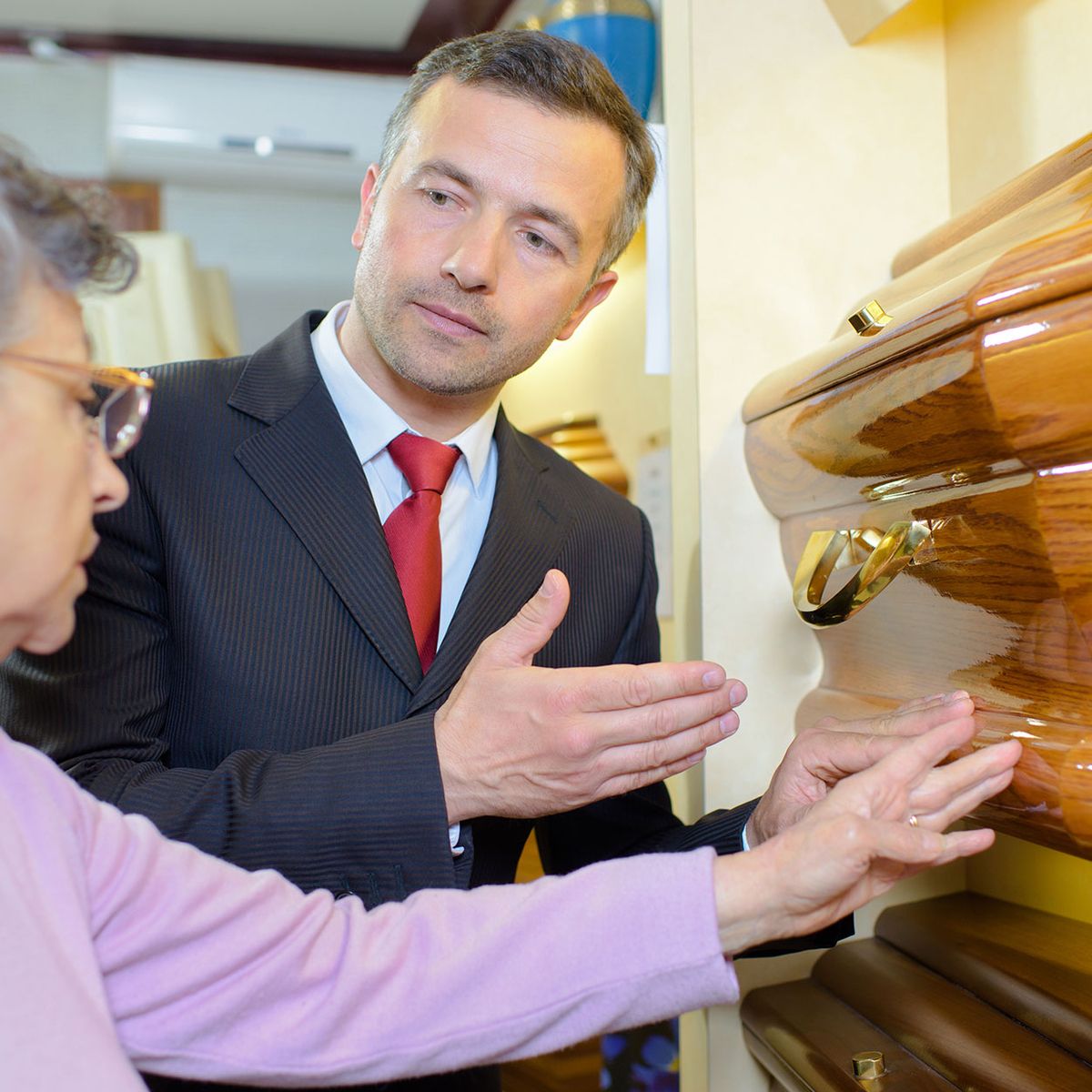 Ein Mann zeigt einer älteren Frau einen Sarg